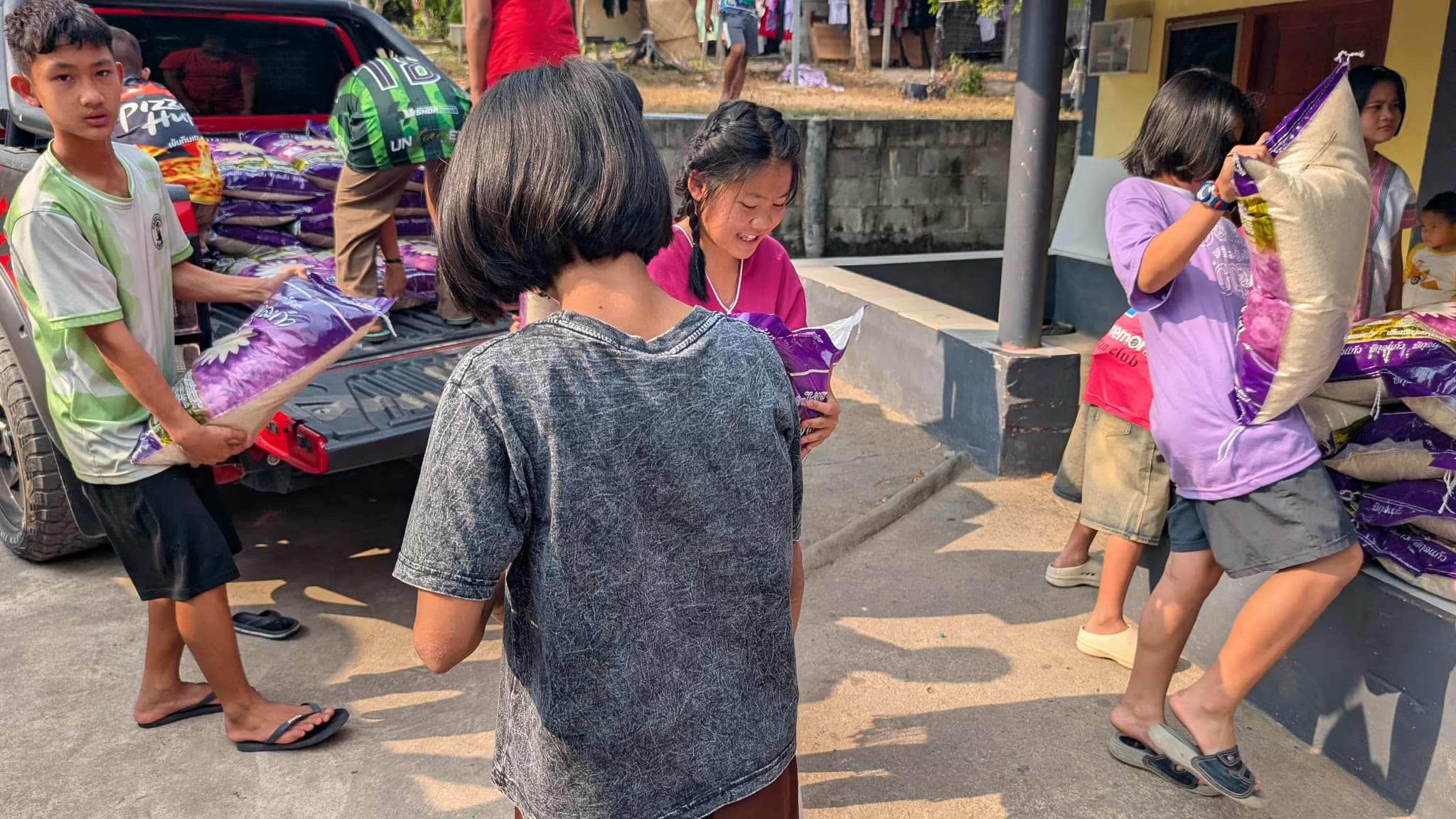 A boy dragging a sack of rice from a truck bed while a girl carries another sack on her shoulder